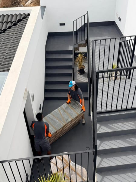 Dos miembros del equipo bajando un mueble embalado por una escalera exterior