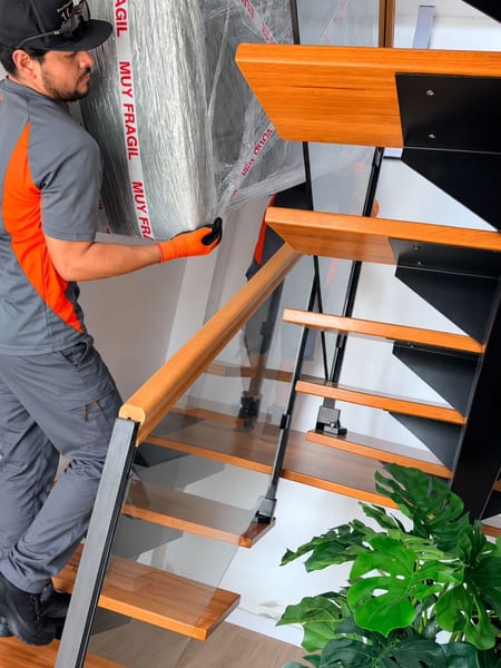 Miembros del equipo bajando un mueble marcado como muy frágil por una escalera interior